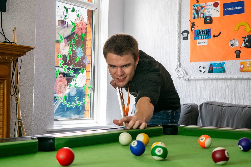 a student playing pool and smiling at the camera