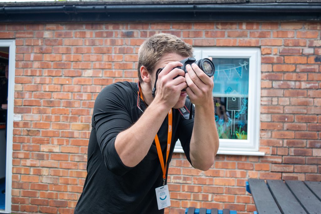 a student taking a photo using a camera stood in front of a brick wall