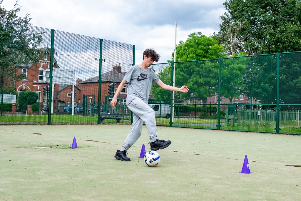 a student playing football, dribbling around cones
