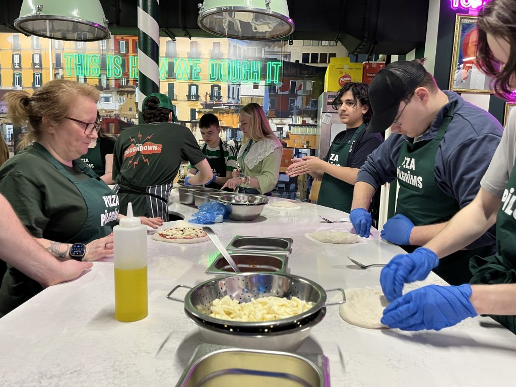 A group of students working on stretching dough on a marble countertop in a colorful vibrant kitchen. 