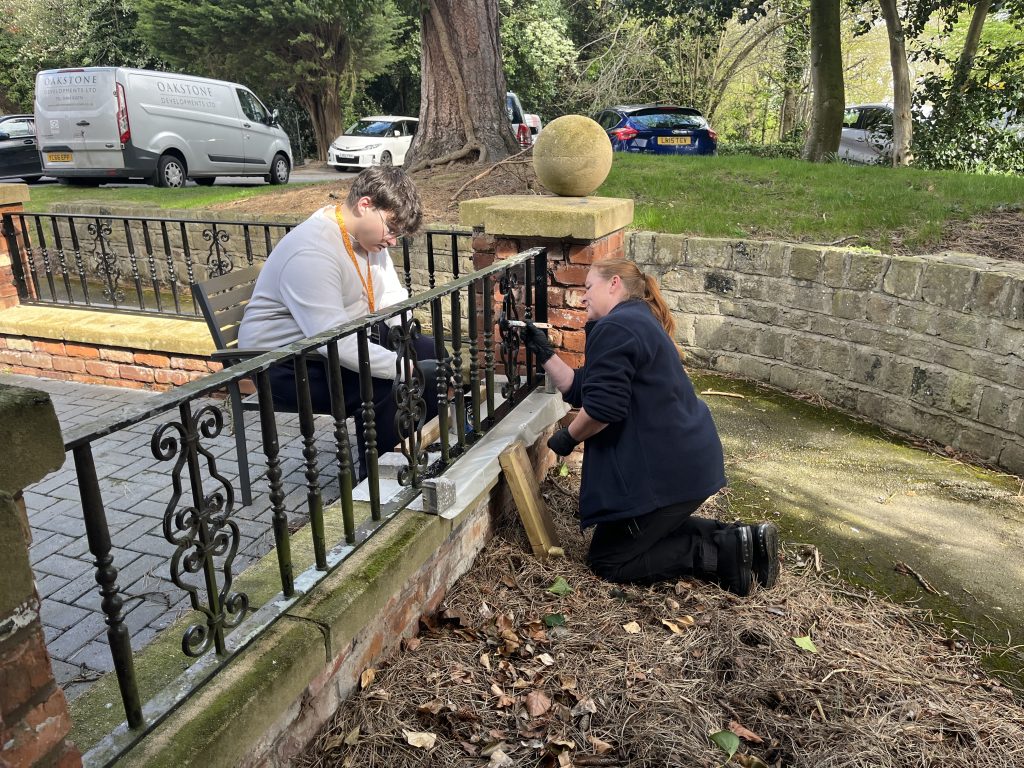 a teen boy paints a fence during work experience alongside a maintenance worker at the Village Hotel cheadle